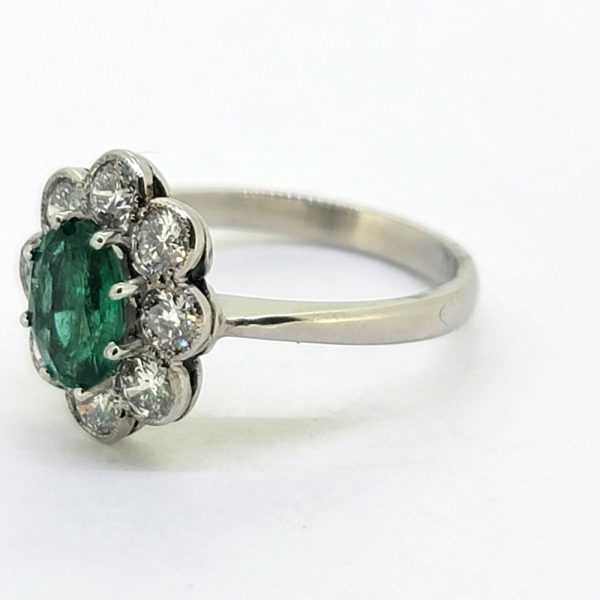 1.10ct Emerald and Diamond Floral Cluster Engagement Ring, 1.10ct oval emerald surrounded by 0.96cts round brilliant-cut diamonds in classic flower design in 18ct white gold