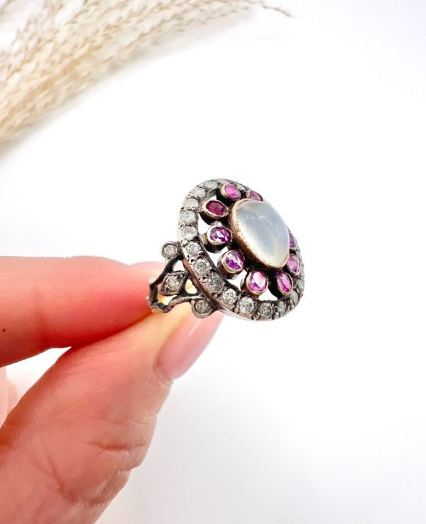 Early Victorian Antique Moonstone Ruby and Diamond Cluster Ring, oval cabochon moonstone surrounded by ruby petals within outer halo border of old-cut diamonds in silver to 18ct yellow gold. Mid 19th century Circa 1865