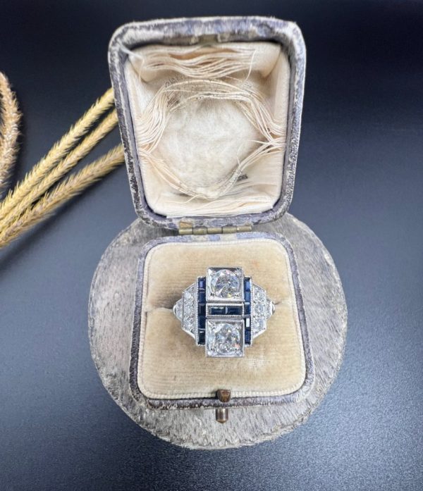Art Deco Style Sapphire and Diamond Geometric Plaque Ring, two round brilliant cut diamonds in square bezel settings bordered by calibre sapphires in 18ct white gold with diamond stepped shoulders