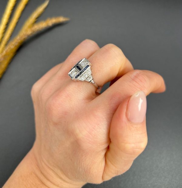 Art Deco Style Sapphire and Diamond Geometric Plaque Ring, two round brilliant cut diamonds in square bezel settings bordered by calibre sapphires in 18ct white gold with diamond stepped shoulders