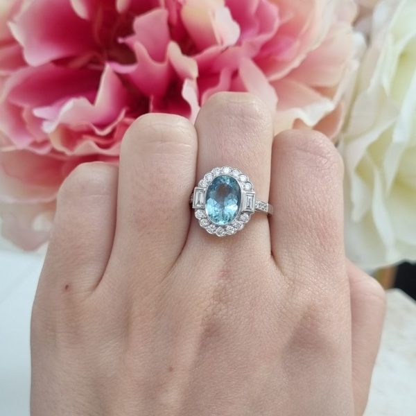 A vintage inspired ring with a 2.10 carat oval aquamarine in the centre surrounded by 0.55 carats of diamonds, rubover set in 18ct white gold.