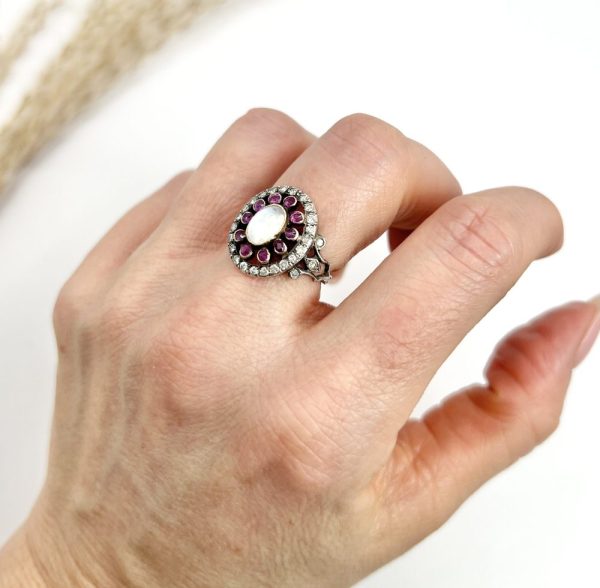Early Victorian Antique Moonstone Ruby and Diamond Cluster Ring, oval cabochon moonstone surrounded by ruby petals within outer halo border of old-cut diamonds in silver to 18ct yellow gold. Mid 19th century Circa 1865
