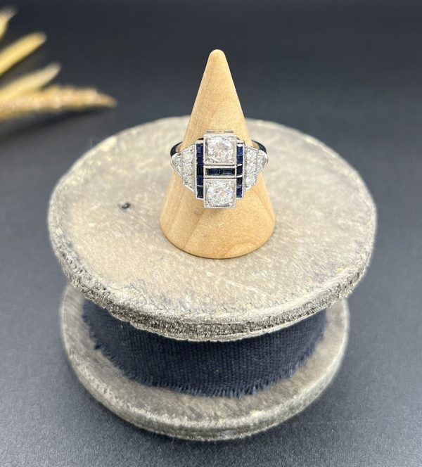 Art Deco Style Sapphire and Diamond Geometric Plaque Ring, two round brilliant cut diamonds in square bezel settings bordered by calibre sapphires in 18ct white gold with diamond stepped shoulders