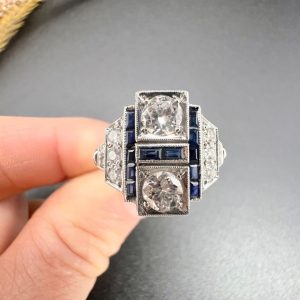 Art Deco Style Sapphire and Diamond Geometric Plaque Ring, two round brilliant cut diamonds in square bezel settings bordered by calibre sapphires in 18ct white gold with diamond stepped shoulders