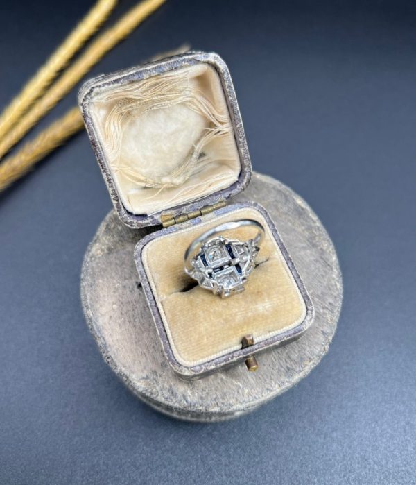 Art Deco Style Sapphire and Diamond Geometric Plaque Ring, two round brilliant cut diamonds in square bezel settings bordered by calibre sapphires in 18ct white gold with diamond stepped shoulders