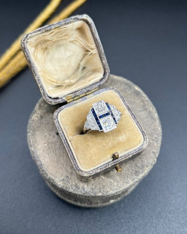 Art Deco Style Sapphire and Diamond Geometric Plaque Ring, two round brilliant cut diamonds in square bezel settings bordered by calibre sapphires in 18ct white gold with diamond stepped shoulders