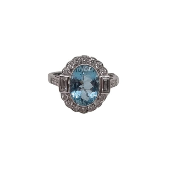 A vintage inspired ring with a 2.10 carat oval aquamarine in the centre surrounded by 0.55 carats of diamonds, rubover set in 18ct white gold.