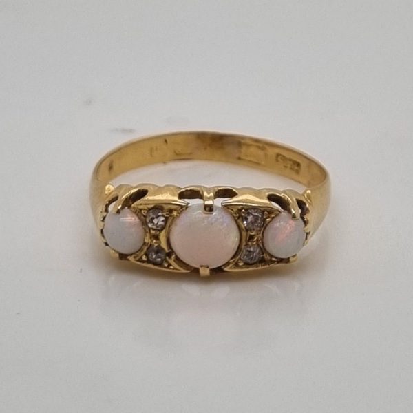 An antique 18ct yellow gold ring featuring three round opal cabochons with four small diamonds set between them in a classic design