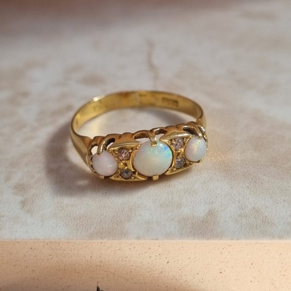 An antique 18ct yellow gold ring featuring three round opal cabochons with four small diamonds set between them in a classic design