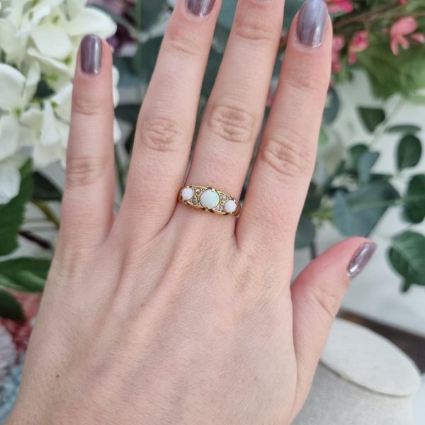 An antique 18ct yellow gold ring featuring three round opal cabochons with four small diamonds set between them in a classic design