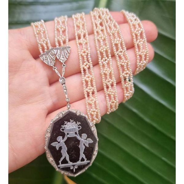 Antique Onyx and Rock Crystal Intaglio Pendant on Seed Pearl Sautoir Necklace, long geometric strung seed pearls suspends oval black onyx and rock crystal intaglio pendant featuring two winged cherubs holding aloft  flowers in an urn