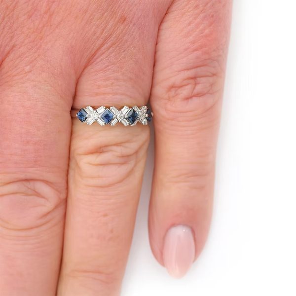 Contemporary 18ct white gold half eternity ring with square-cut blue sapphires and baguette and brilliant-cut diamonds in a geometric design.