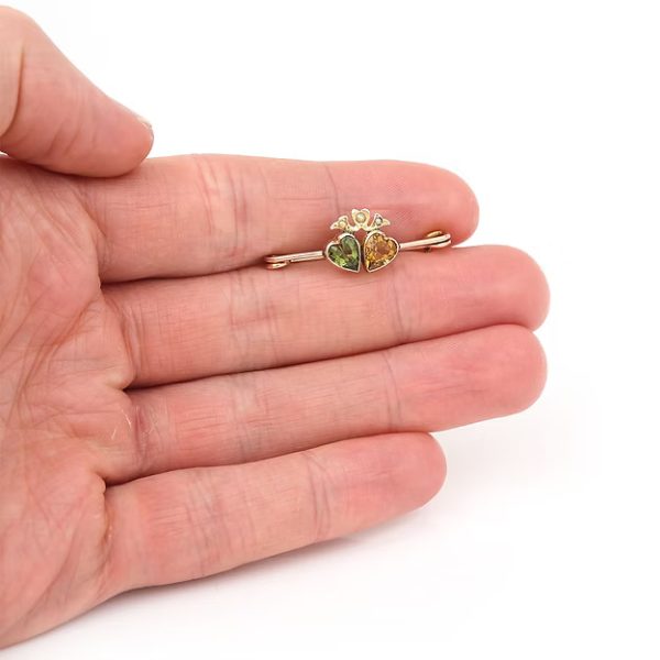 Edwardian 9ct gold brooch featuring twin hearts set with peridot and citrine, topped with a floral crown motif adorned with split pearls, circa 1910