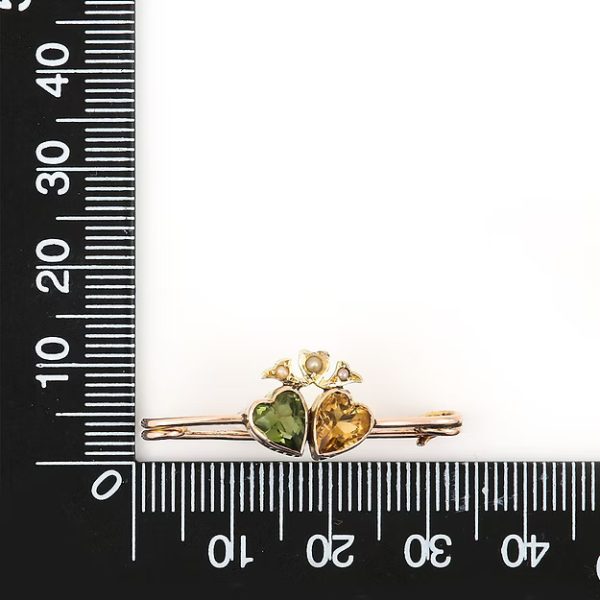 Edwardian 9ct gold brooch featuring twin hearts set with peridot and citrine, topped with a floral crown motif adorned with split pearls, circa 1910