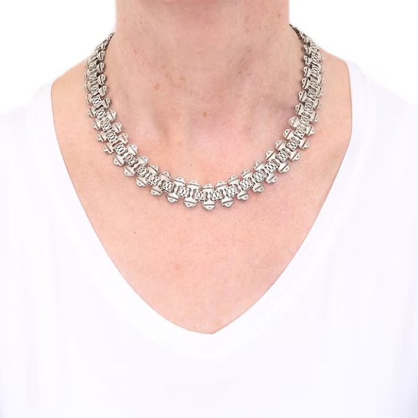 Victorian silver collar necklace featuring engraved flat links, foliate connectors, and heart-shaped details, circa 1880.