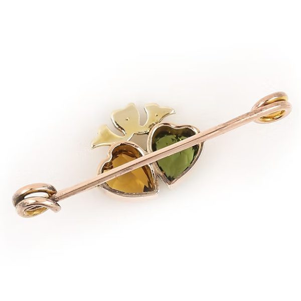 Edwardian 9ct gold brooch featuring twin hearts set with peridot and citrine, topped with a floral crown motif adorned with split pearls, circa 1910