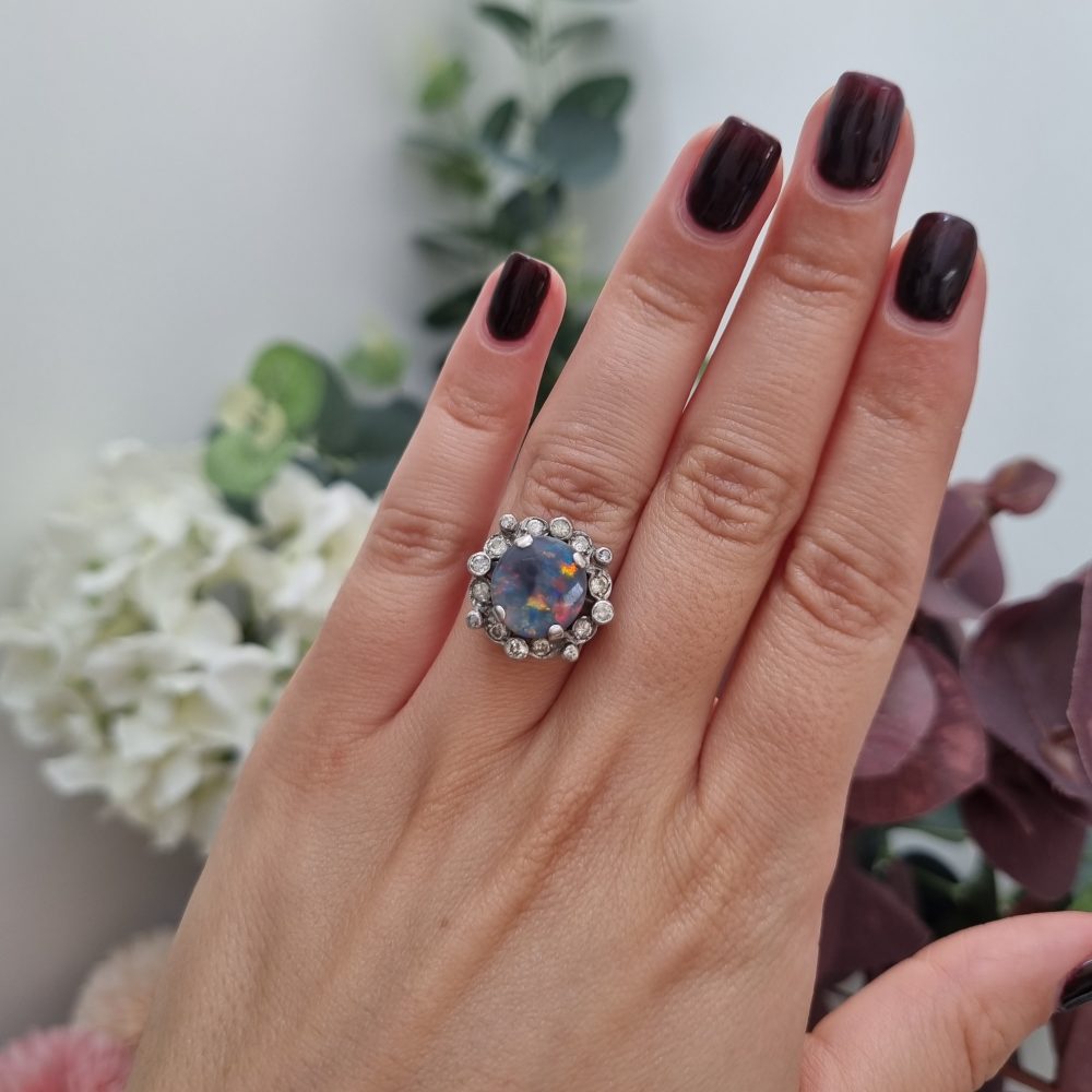 Vintage black opal and diamond cluster ring in platinum, featuring a circular black opal cabochon surrounded by a halo of 16 round-cut diamonds.