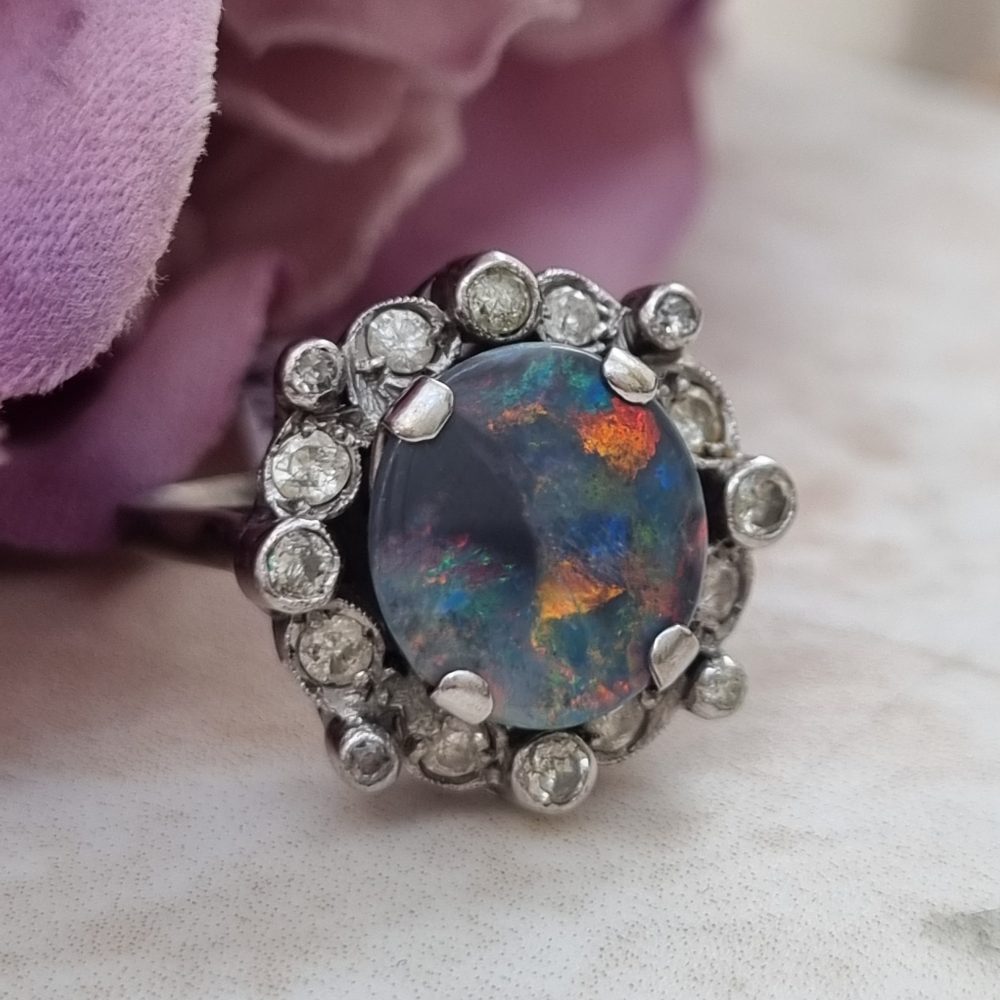 Vintage black opal and diamond cluster ring in platinum, featuring a circular black opal cabochon surrounded by a halo of 16 round-cut diamonds.