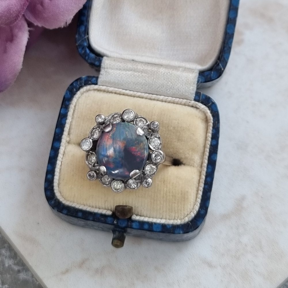 Vintage black opal and diamond cluster ring in platinum, featuring a circular black opal cabochon surrounded by 16 round-cut diamonds.