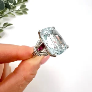Vintage Cushion Cut Aquamarine Cocktail Ring with Ruby Shoulders in Platinum, 12ct cushion-cut aquamarine on reeded platinum band set with calibre red rubies. Circa 1960s