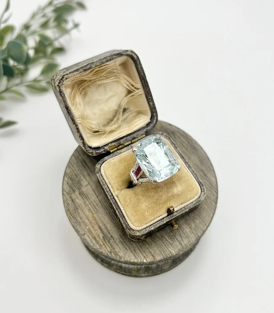 Vintage Cushion Cut Aquamarine Cocktail Ring with Ruby Shoulders in Platinum, 12ct cushion-cut aquamarine on reeded platinum band set with calibre red rubies. Circa 1960s