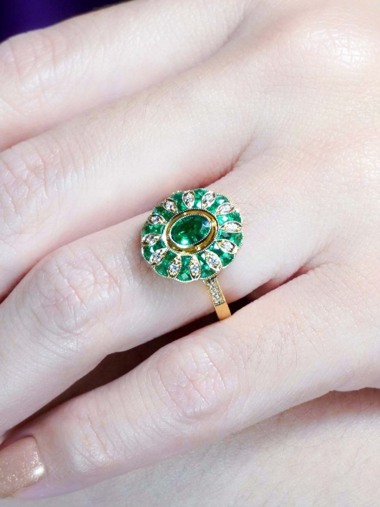 Modern Emerald and Diamond Oval Cluster Ring in 18ct Yellow Gold, vivid oval emerald encircled by alternating emeralds and diamonds in floral pattern